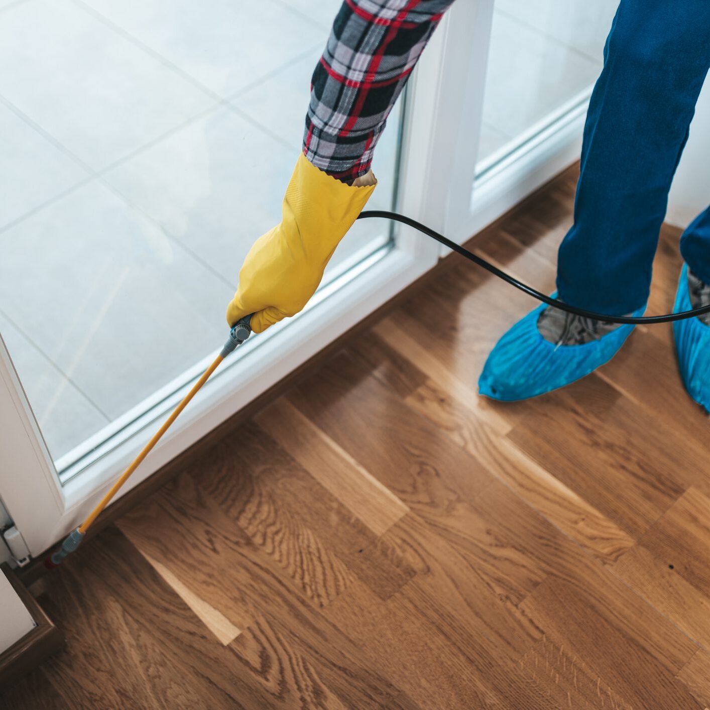 Professional exterminator in protective workwear spraying pesticide in apartment kitchen.